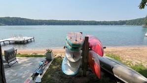 Un ambiente lacustre con kayak e tavole da paddleboard, un molo in cemento e vista sul lago e alberi sullo sfondo.