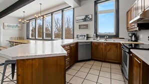 A modern kitchen with a large island, wooden cabinets, and a view of trees through the windows. - Northview Blue Mountain (blue mountains)