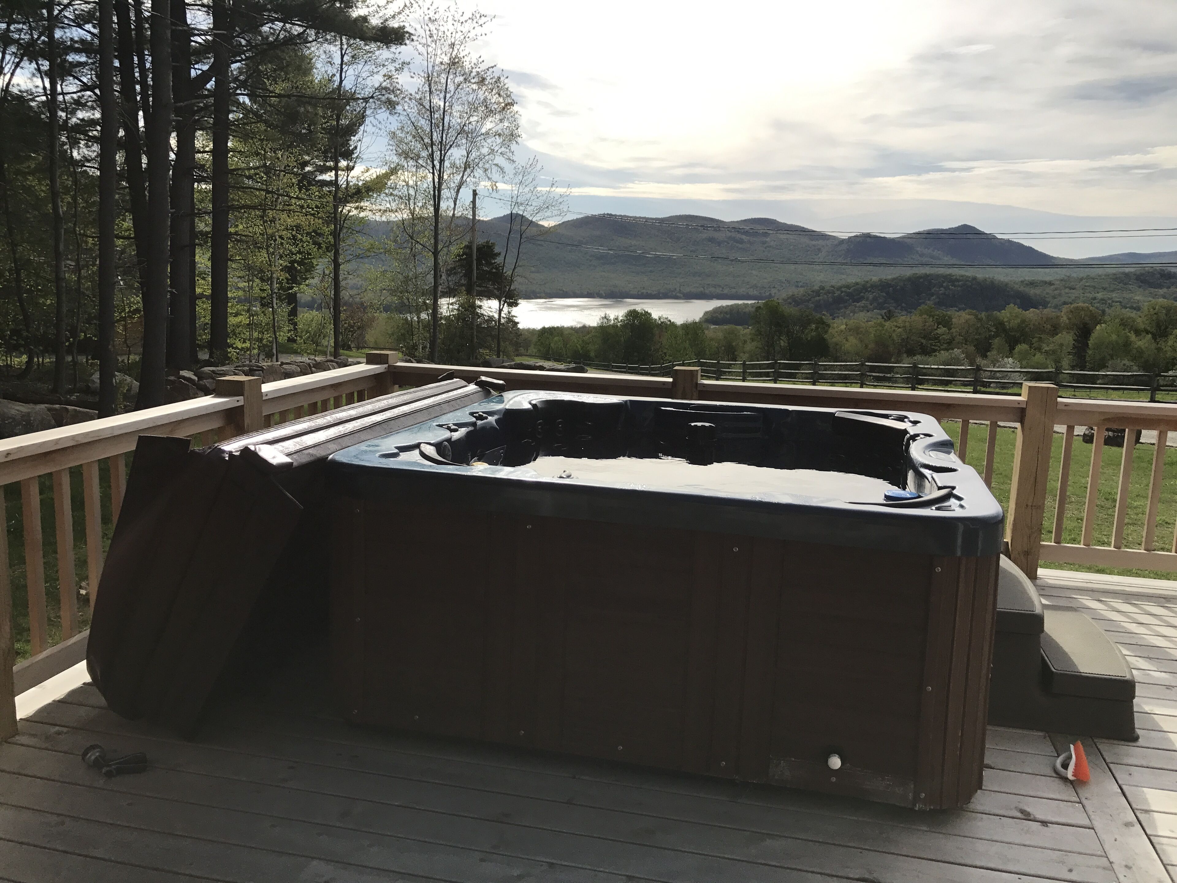 Un jacuzzi en una terraza de madera con vistas a montañas y un lago.