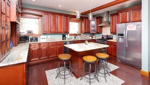 A spacious kitchen with wooden cabinets, a large island with stools, a refrigerator, and a microwave. - Luxury Mountain Home with Hot Tub, Sauna & Views — Walk to Mountain Top Inn (Chittenden)