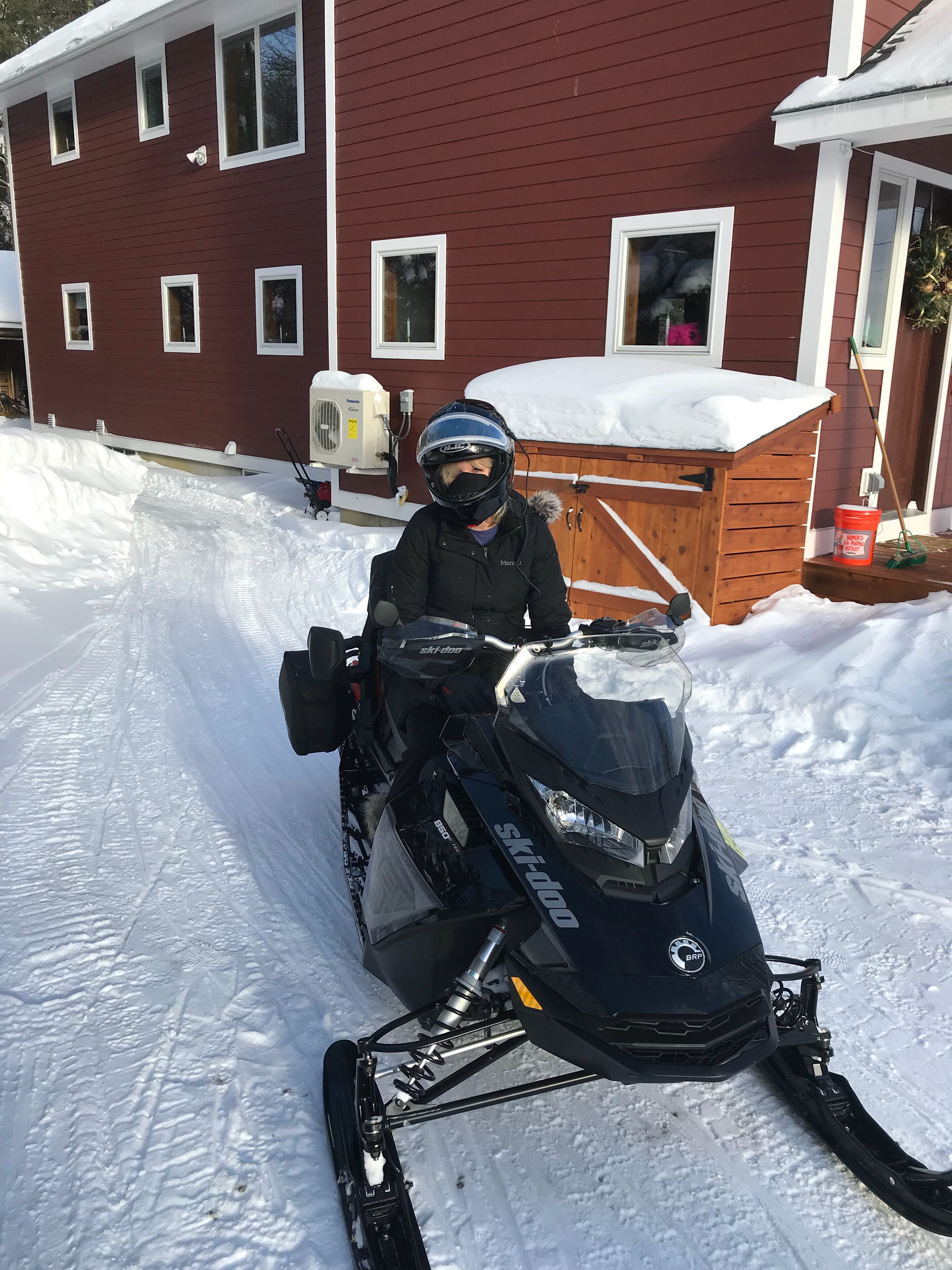 A snowmobile parked in front of a red house with a wooden deck and a snow-covered roof.
