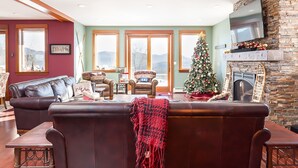 A cozy living room with a leather sofa, a Christmas tree, and a fireplace. - Luxury Mountain Home with Hot Tub, Sauna & Views — Walk to Mountain Top Inn (Chittenden)