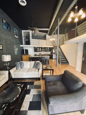 A modern living room with a sofa, coffee table, and a dining area with a staircase. - Up to 50% off!!! Spacious & Clean Loft! Downtown right out the Front Door (Nashville)