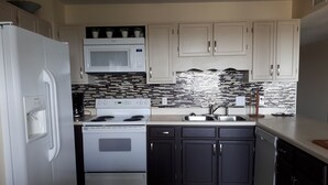 A compact kitchen with white appliances, a tiled backsplash, and dark cabinets. - Weeks in September still available! Book now for a great vacation. (Myrtle Beach)