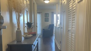 A hallway with a wooden floor, a table with a vase and a plant, a chair, and a door with a thermostat. - Weeks in September still available! Book now for a great vacation. (Myrtle Beach)