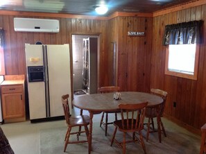 Un intérieur en bois comprenant un coin cuisine, avec un réfrigérateur, une table à manger avec des chaises, et un panneau indiquant « APPÂTS VIVANTS ».