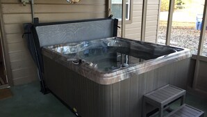 Un bain à remous avec un revêtement extérieur en bois, un petit banc en bois et une fenêtre donnant sur l’extérieur.