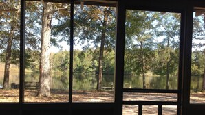 Une vue à travers la fenêtre d’une cabane, avec un lac et des arbres en arrière-plan.