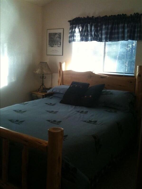 A bedroom with a bed, a nightstand, a lamp, a window with blinds, and a framed picture on the wall. - Texas House: Mountain Home in Ruidoso/Alto Lakes Golf & CC. New Heating & A/C (Alto)