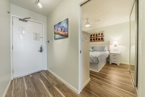 Un pasillo que conduce a un dormitorio con una cama, una mesita de noche y una lámpara de pared.