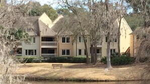 A multi-story building with a symmetrical facade, a central entrance, and a small front yard with a bench. - PANORAMIC GOLF LAGOON VIEW,WALK TO BEACH, BEACH LOCKER,FROM OWNER,NO HIDDEN FEES (Hilton Head Island)