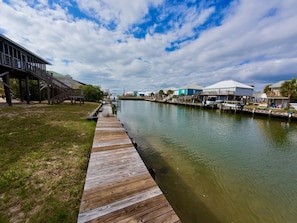 A wooden boardwalk leading to a waterfront area with houses and a covered structure.