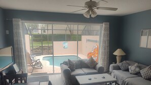 A living room with a sofa, a coffee table, and a TV. There is a pool outside. - 
Orlando Dreams Come True – Private Splash Pool, 3 En-Suite BRs, Near Disney (Kissimmee)
