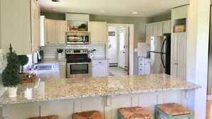 Una cocina con armarios blancos, encimera de granito, electrodomésticos de acero inoxidable y una pequeña planta en maceta.
