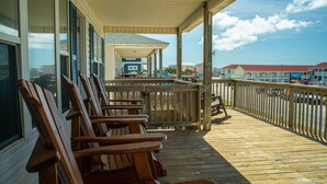 A wooden deck with several chairs, a covered area, and a view of buildings in the background.