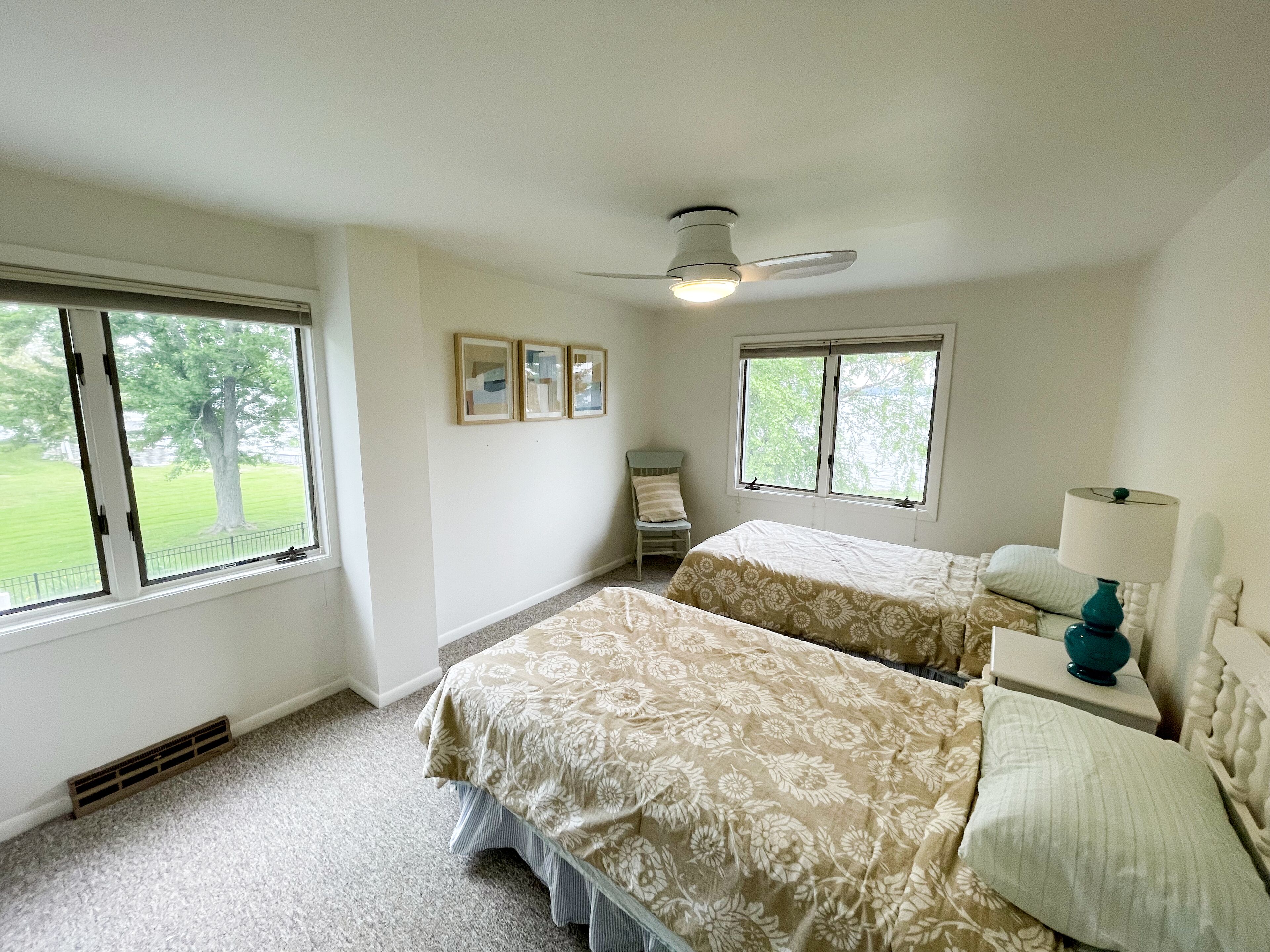 Ein Schlafzimmer mit zwei Betten, einem Deckenventilator und einem Fenster mit Blick auf eine grüne Landschaft.