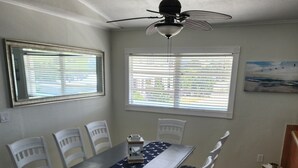 A dining area with a table and chairs, a ceiling fan, and windows with blinds.