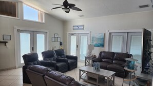 A spacious living room with a ceiling fan, a fireplace, and a view of the beach through the windows.