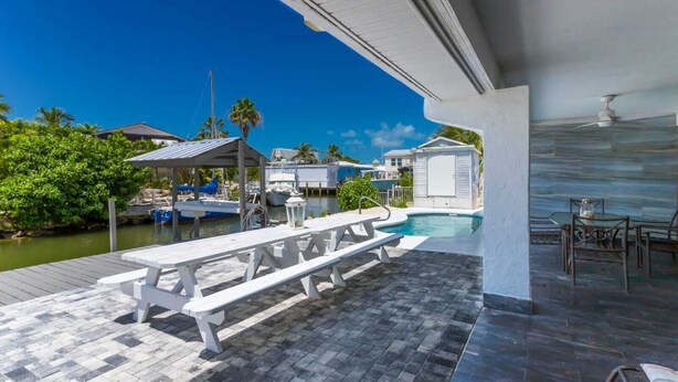 A covered outdoor area with a pool, a picnic table, and a view of the water and boats.