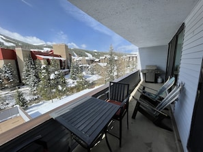 A balcony with a table and chairs, overlooking a snowy landscape with buildings and trees.