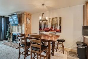 A dining area with a wooden table and chairs, a chandelier, and a painting of trees.