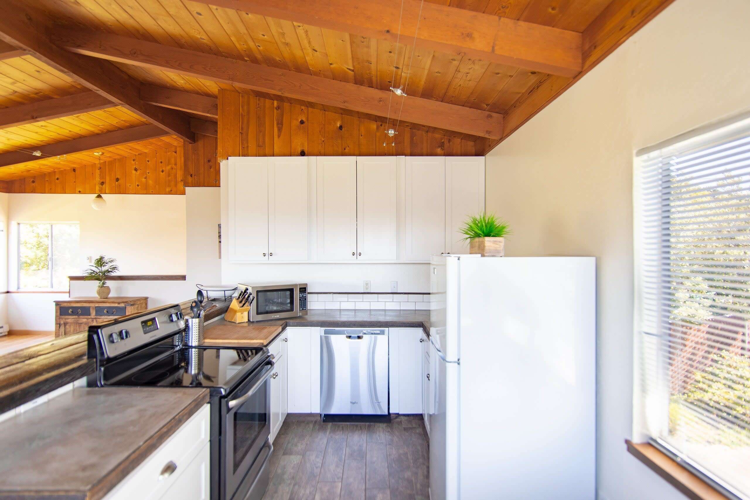 A modern kitchen with white cabinets, stainless steel appliances, and a wooden ceiling.