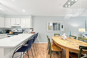 A modern kitchen with white cabinets, a central island, and a dining area with a wooden table and chairs.