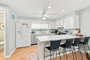 A modern kitchen with white cabinets, a central island with bar stools, a microwave, and a stove.