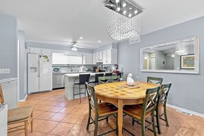 A modern kitchen with white cabinets, a central island, and a dining area with a wooden table and chairs.