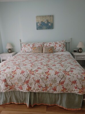 Quarto com colcha florida, duas mesas de cabeceira com abajures, uma obra de arte na parede e parede em azul claro.