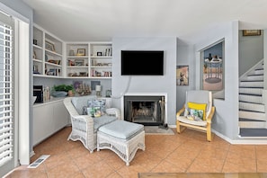 A living room with a fireplace, a television, and a bookshelf filled with books and decorative items.