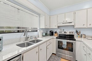 Uma cozinha moderna com armários brancos, eletrodomésticos de aço inoxidável e uma janela com persianas.