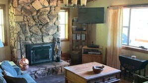 Ein gemütliches Wohnzimmer mit Kamin aus Stein, Holzbalkendecke und einem wandmontierten Flachbildfernseher.