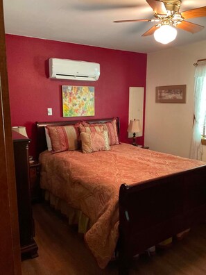 A bedroom with a bed, an air conditioner, a ceiling fan, a painting, and a window with curtains. - Rent for Labor Day! Magnificent View! By golf course! Rates are very affordable! (Cloudcroft)