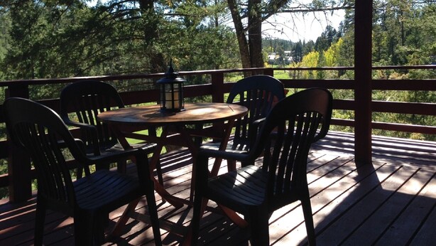 Eine Holzterrasse mit einem runden Tisch und Stühlen, umgeben von Bäumen.