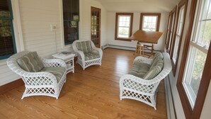 Ein Zimmer mit weißen Korbmöbeln, darunter zwei Stühle und ein Sofa, angeordnet um einen Holztisch.