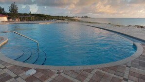 En swimmingpool med ett kaklat poolområde, omgiven av en strand och en molnig himmel.