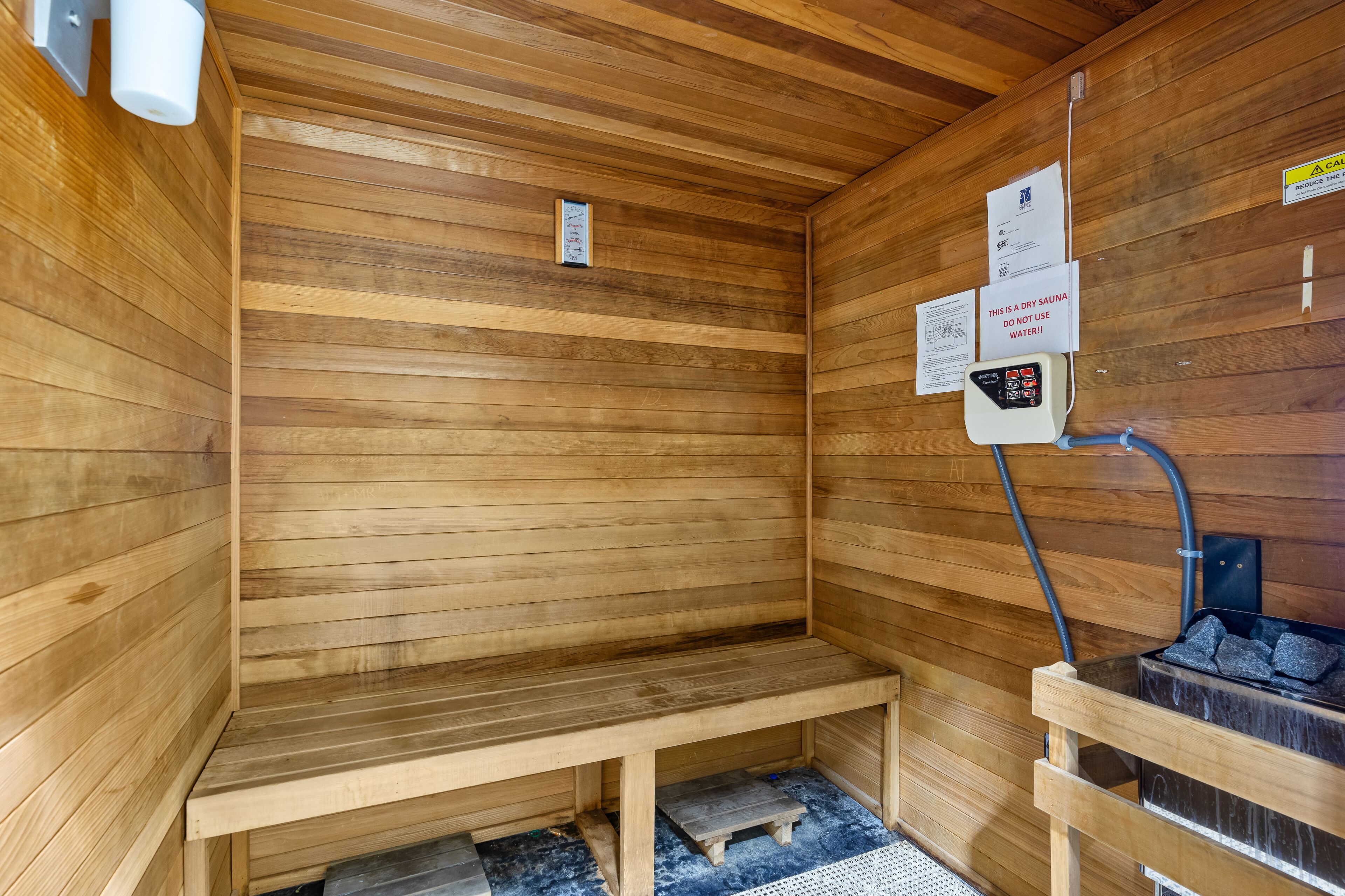 Una sauna con paredes de madera, un banco, un calentador y carteles informativos.