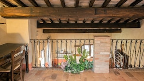 Interior rústico com vigas de madeira aparentes, parede de tijolos e portão de ferro forjado.