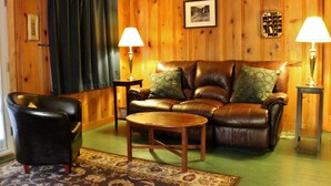 Una sala de estar acogedora con un sofá de cuero, un sillón a juego, una mesa de centro de madera y dos lámparas sobre mesitas de noche.