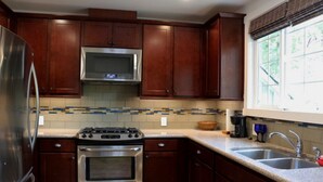 Una cocina con armarios de madera, un refrigerador de acero inoxidable, un microondas, una estufa y un lavamanos.