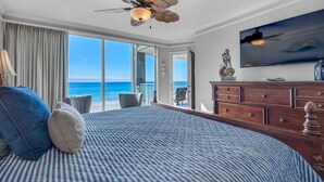 Habitación de hotel con una cama grande, ventilador de techo, televisor y vista al océano.