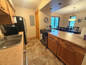 A kitchen with a stainless steel sink, a black refrigerator, a stove, and wooden cabinets.