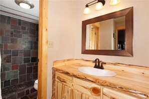 A bathroom with a stone wall, a wooden vanity with a white sink, and a mirror with three lights. - 2 blocks to Main Street - Easy access to ski Copper/Breckenridge - Virtual Tour (Frisco)