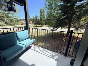 A balcony with a blue sofa, a metal railing, and a view of a residential area with trees and a clear sky.