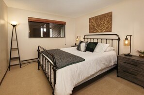A bedroom with a bed, bedside tables, a ladder, a window, and a wall art piece.