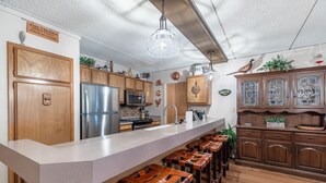 Una cocina con gabinetes de madera, un refrigerador de acero inoxidable, una barra con taburetes y una lámpara colgante.