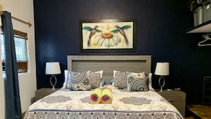 A bedroom with a large bed, patterned bedding, two bedside lamps, and a painting of hummingbirds on the wall. - Villa Papaya, 2 bedrooms, specious, comfortable home, beach walkable. (San Francisco)