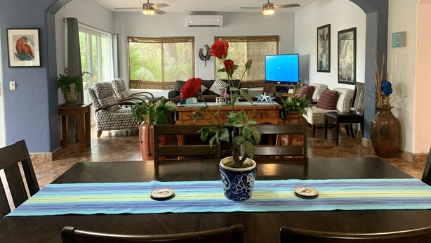 A dining area with a table set for four, a television in the background, and a large window with a view of greenery. - Villa Papaya, 2 bedrooms, specious, comfortable home, beach walkable. (San Francisco)