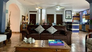 A living room with a brown sofa, patterned cushions, a wooden coffee table with decorative items, and a view into the kitchen area. - Villa Papaya, 2 bedrooms, specious, comfortable home, beach walkable. (San Francisco)
